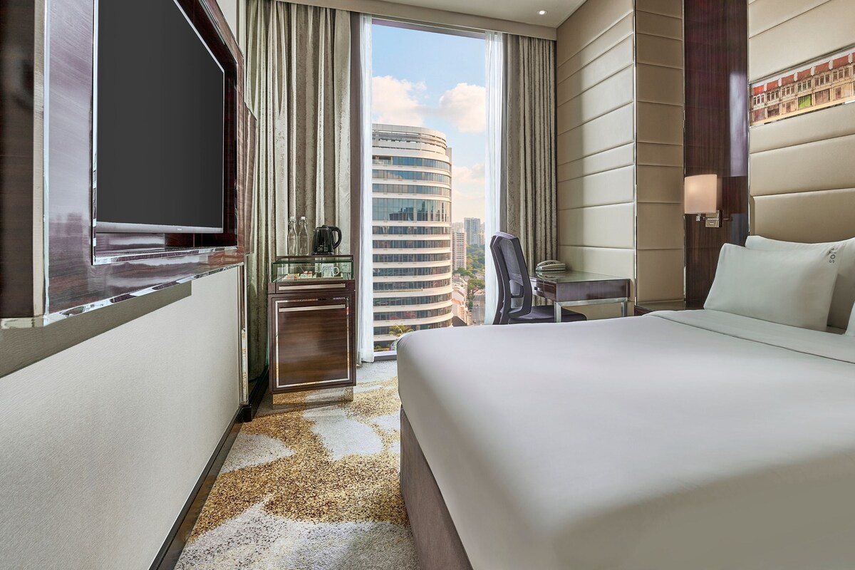 Habitación de hotel con cama, televisión, minibar, escritorio y vista a la ciudad.