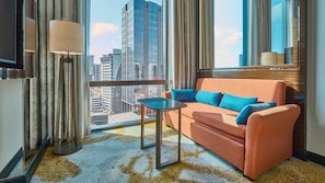 Une chambre d’hôtel moderne, dotée d’un canapé, d’une petite table et offrant une vue sur les bâtiments de la ville.