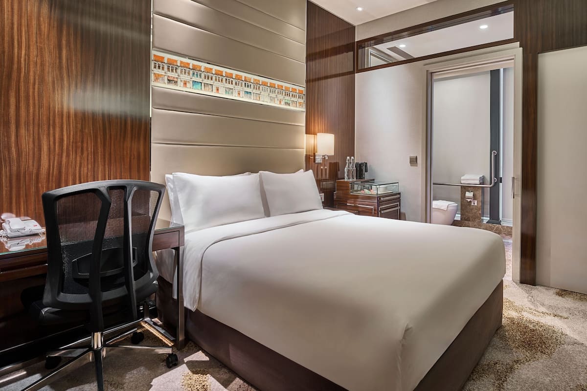 Habitación de hotel con cama, escritorio, silla y baño visible a través de una puerta abierta.