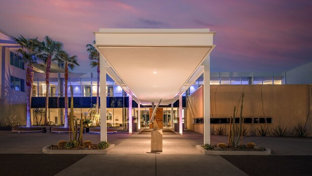 A modern building with a covered entrance, palm trees, and cacti.