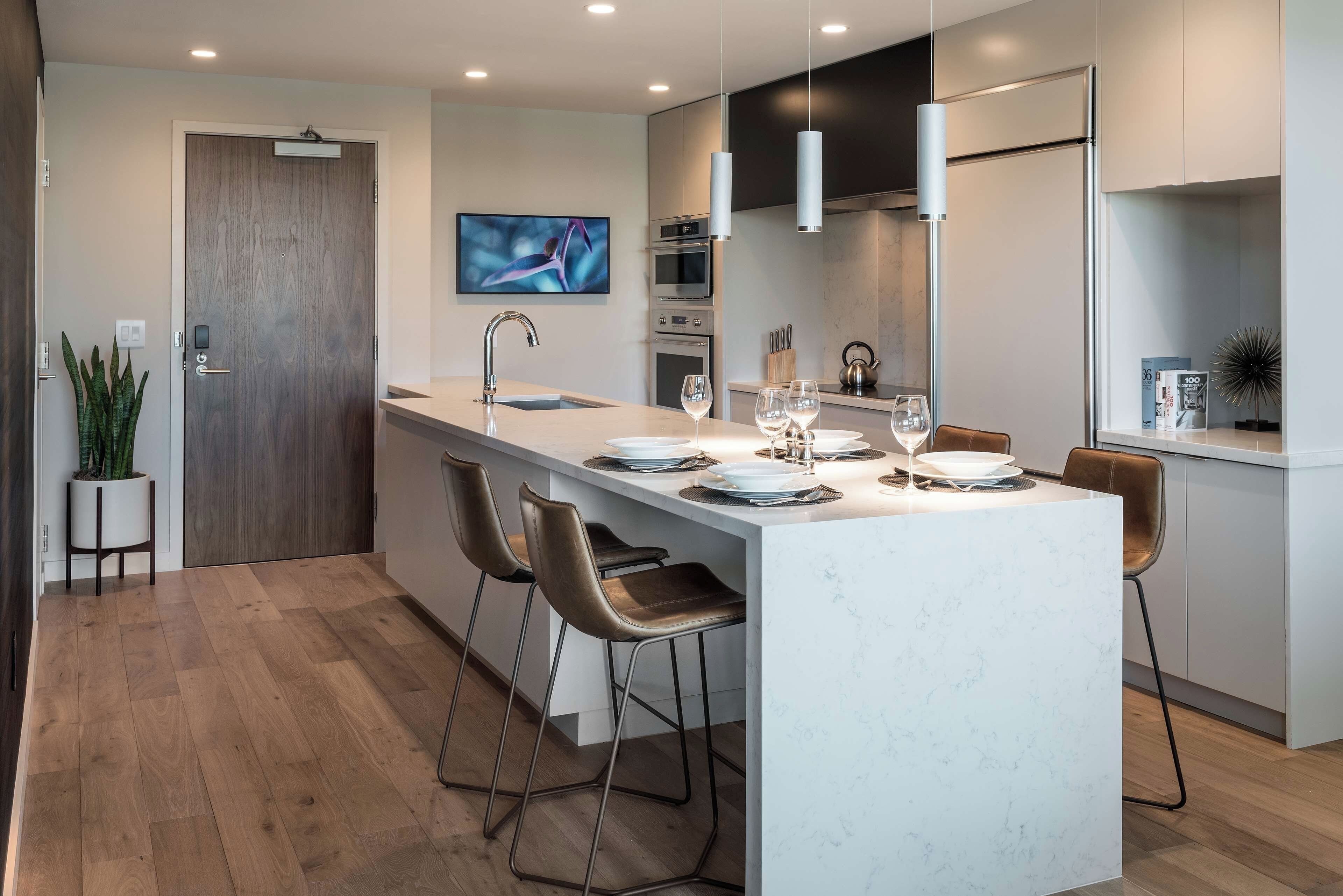 A modern kitchen with a central island, bar stools, a built-in oven, and a flat-screen TV.