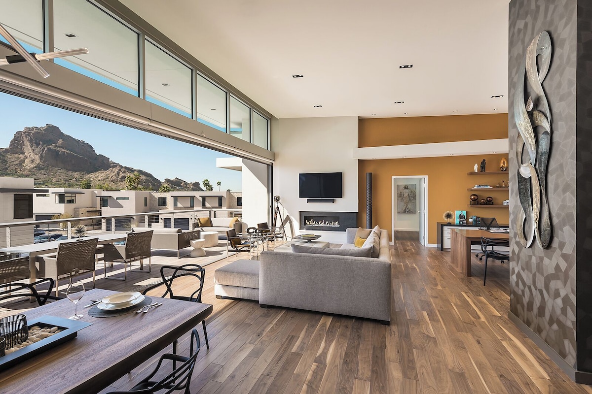 A spacious living area with a fireplace, a dining area with a wooden table, and a view of a mountainous landscape through large windows.