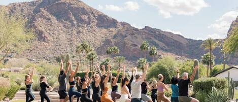 Un grupo de personas practicando yoga al aire libre con montañas al fondo.