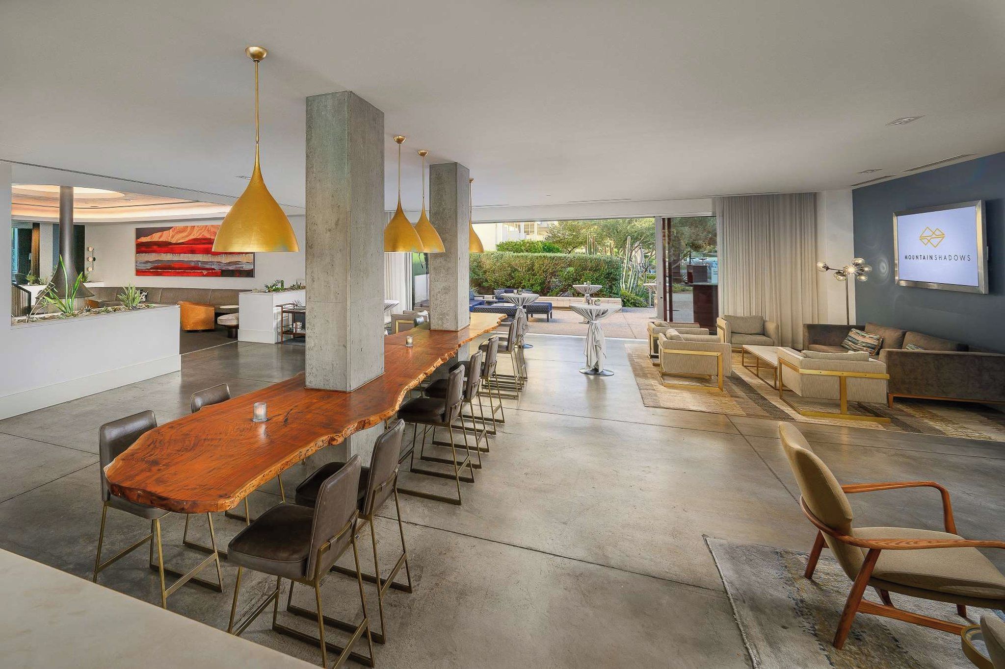 A modern interior with a long wooden bar, multiple seating areas, and a large window offering a view of the outdoors.