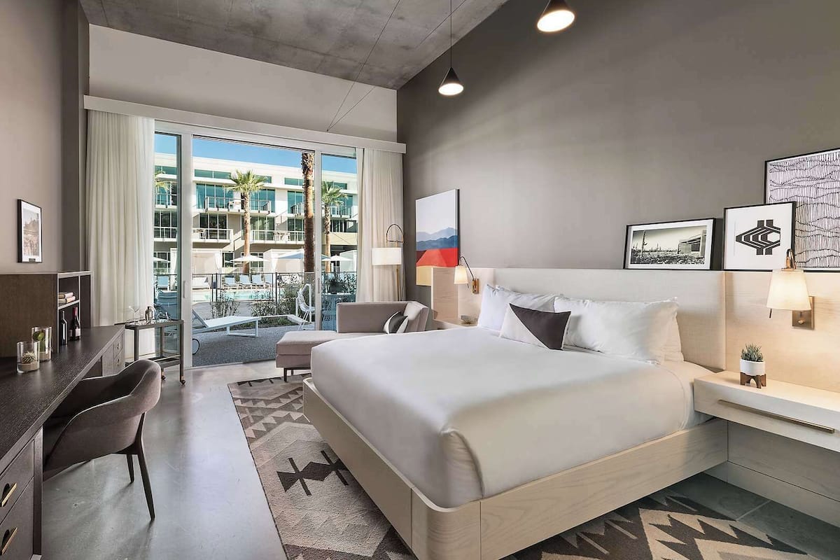 A modern hotel room with a large bed, a desk, and a view of a pool and building.