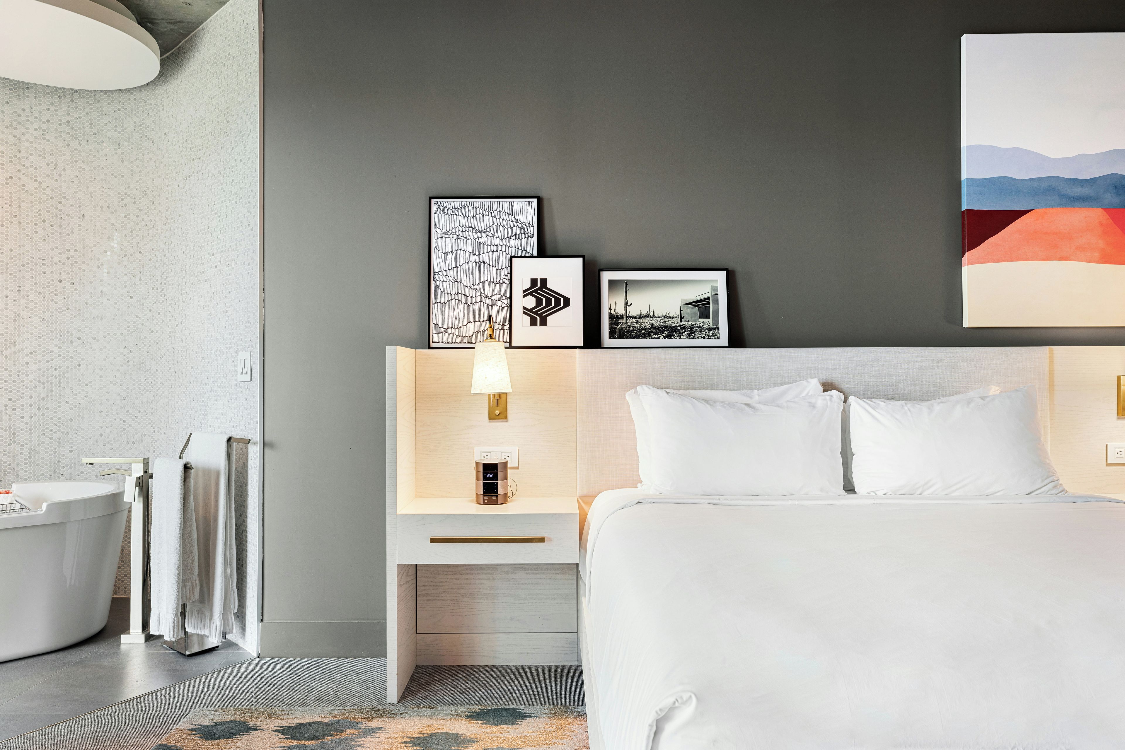 A modern hotel room with a bed, bedside tables, a lamp, a picture frame, and a painting on the wall.