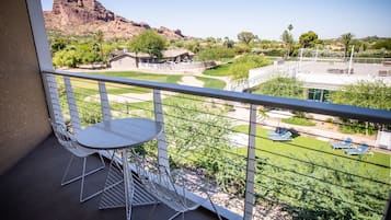 A balcony with a table and chairs, overlooking a well-maintained lawn and a distant mountain.