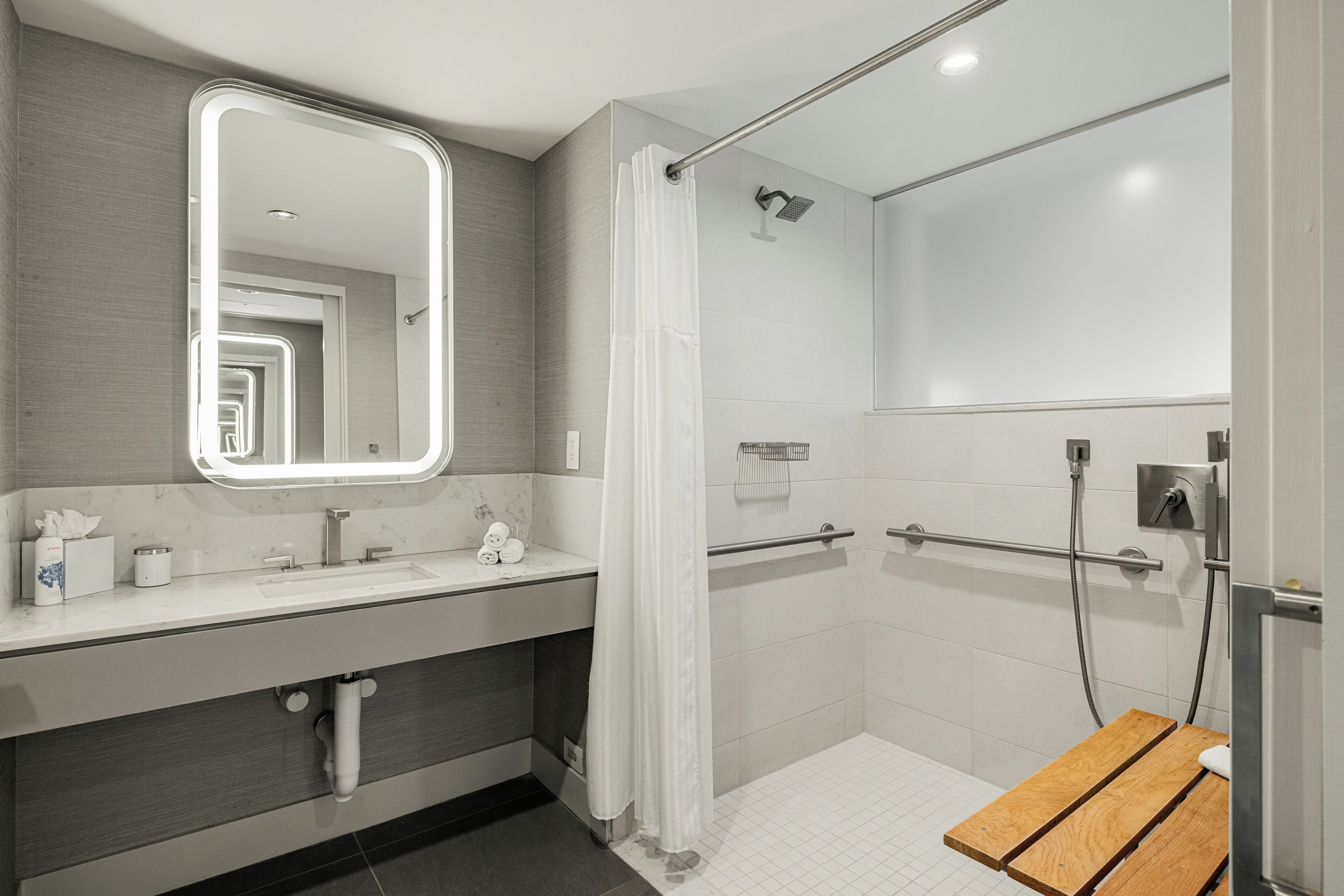 A modern bathroom with a large mirror, a shower, and a wooden bench.