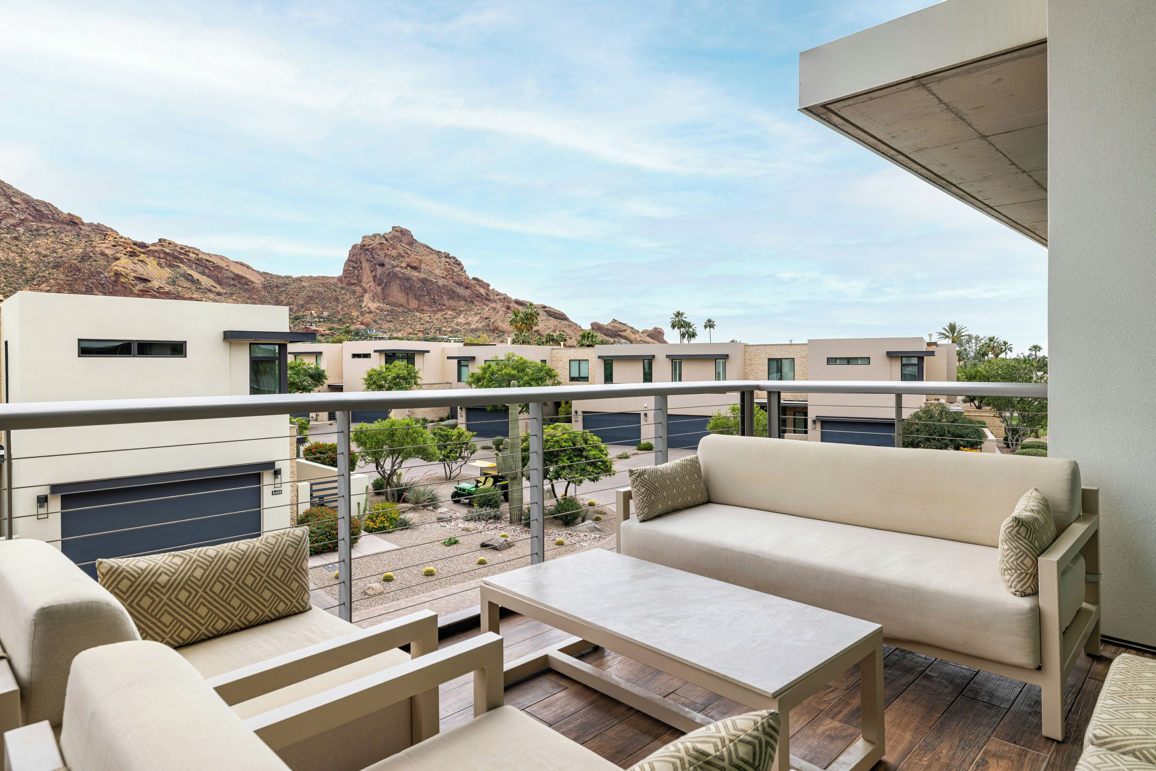 A balcony with outdoor furniture, a view of a desert landscape, and modern buildings in the background.
