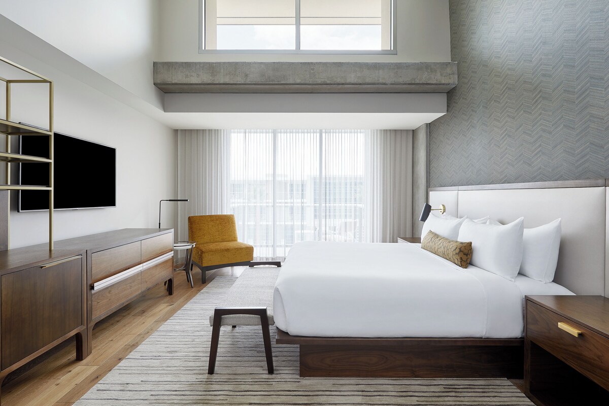 A modern hotel room with a large bed, a television, a desk, and a chair.