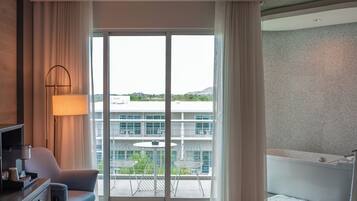 A hotel room with a balcony, a desk with a lamp, a chair, a bed, and a bathtub.