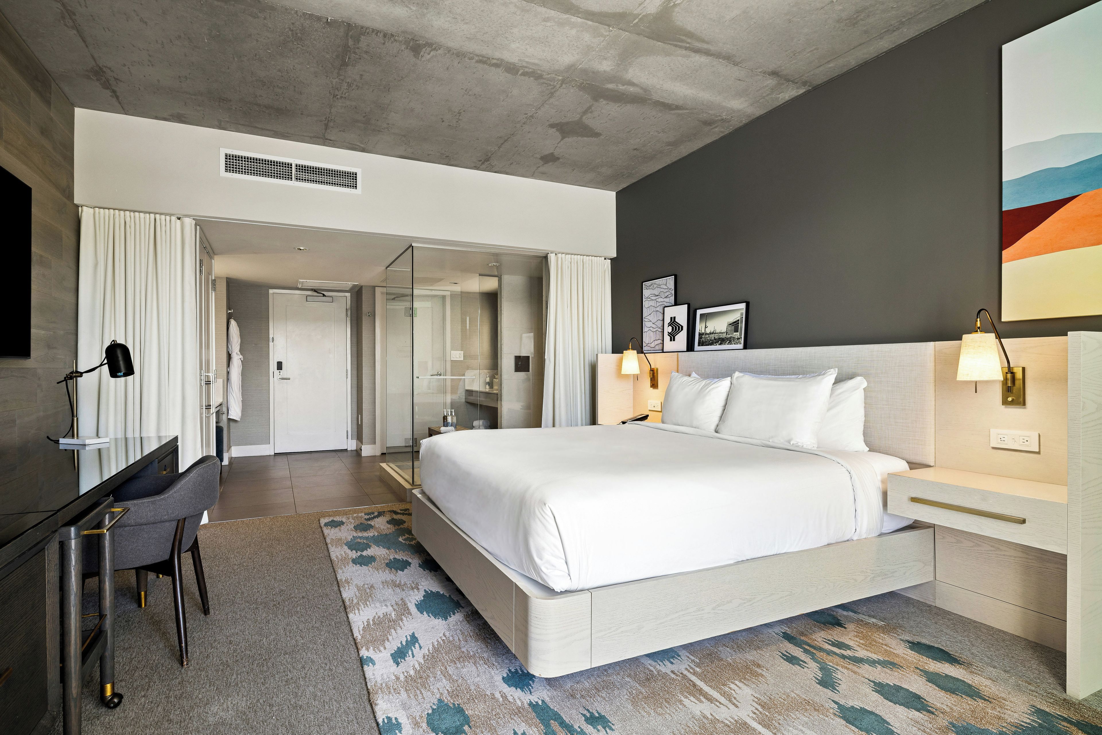A modern hotel room with a large bed, a desk, and a shower area.