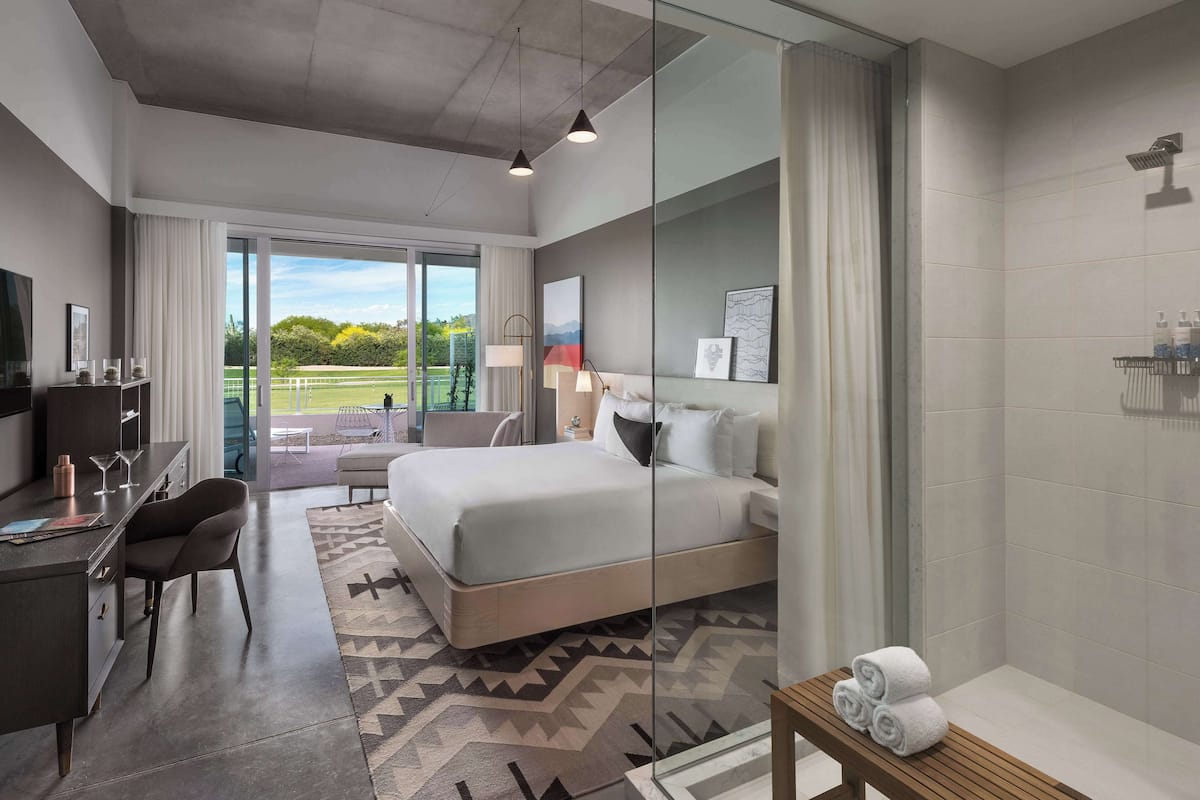 A modern hotel room with a large bed, a desk with a chair, a TV, and a view of a golf course.