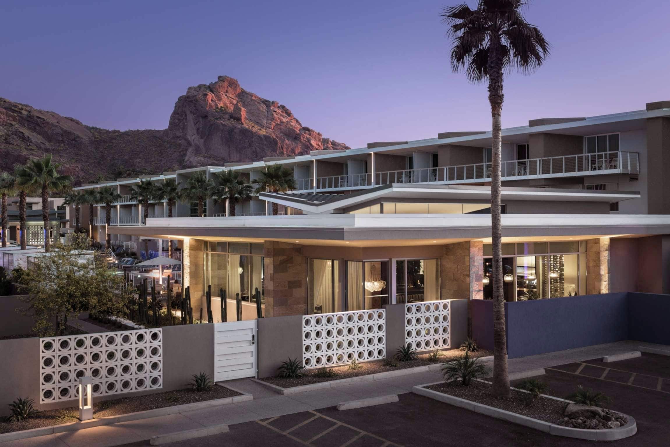 A modern hotel with a two-story structure, outdoor seating, and a view of a mountain.