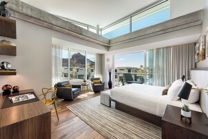 Quarto de hotel moderno com uma cama grande, uma mesa, uma cadeira e uma varanda com vista para as montanhas.