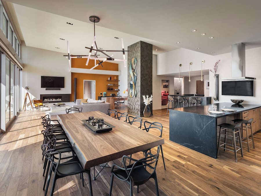 Uma cozinha moderna com uma ilha central, uma área de jantar com uma mesa comprida e um espaço de estar com lareira.