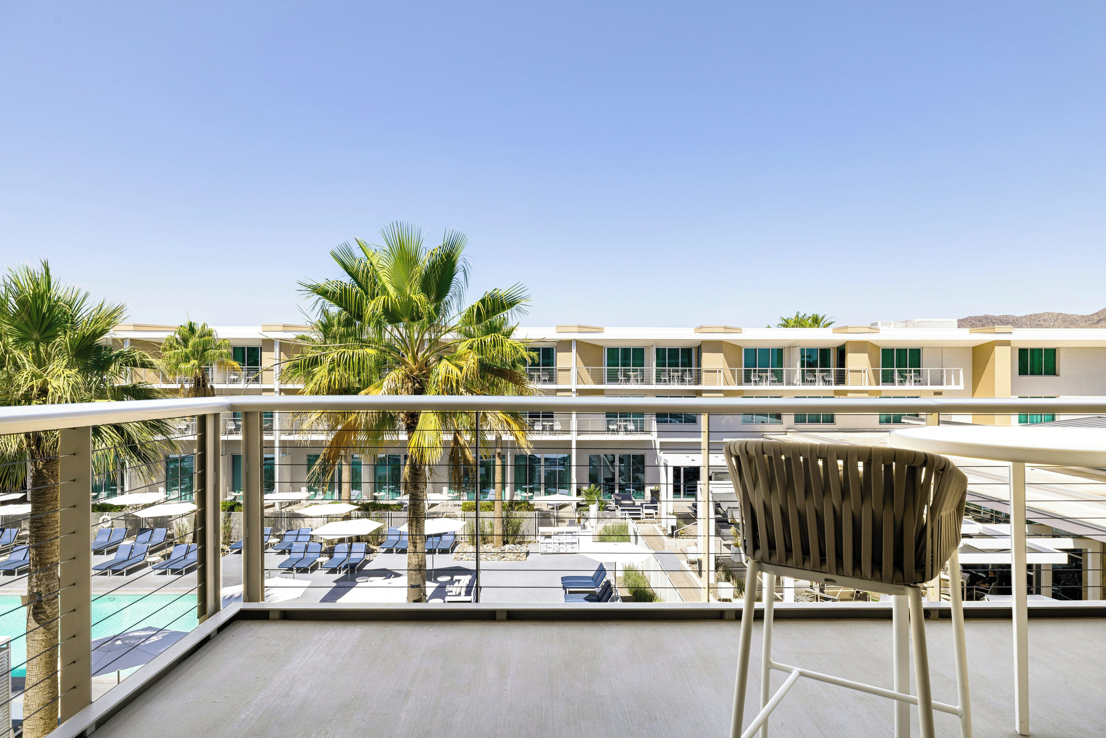 A balcony with a view of a pool area, lounge chairs, and palm trees.
