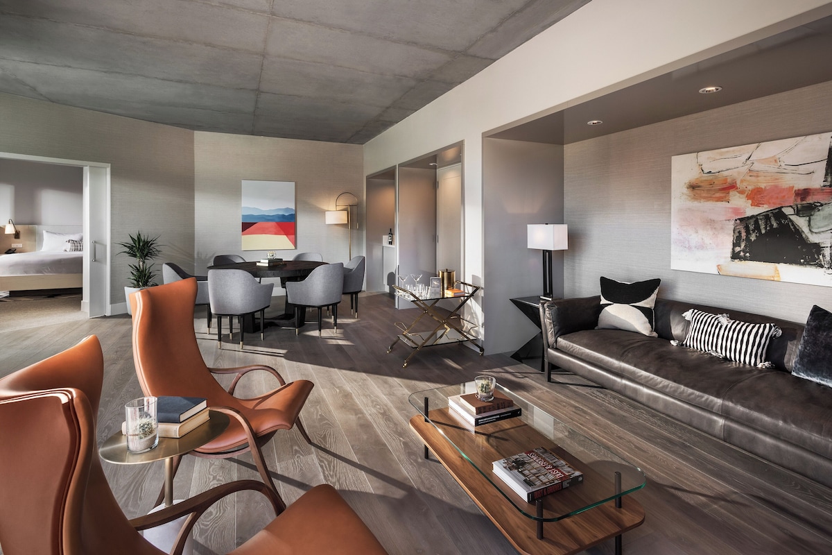 A modern hotel lobby with a seating area, a sofa, a coffee table, and a dining setup.