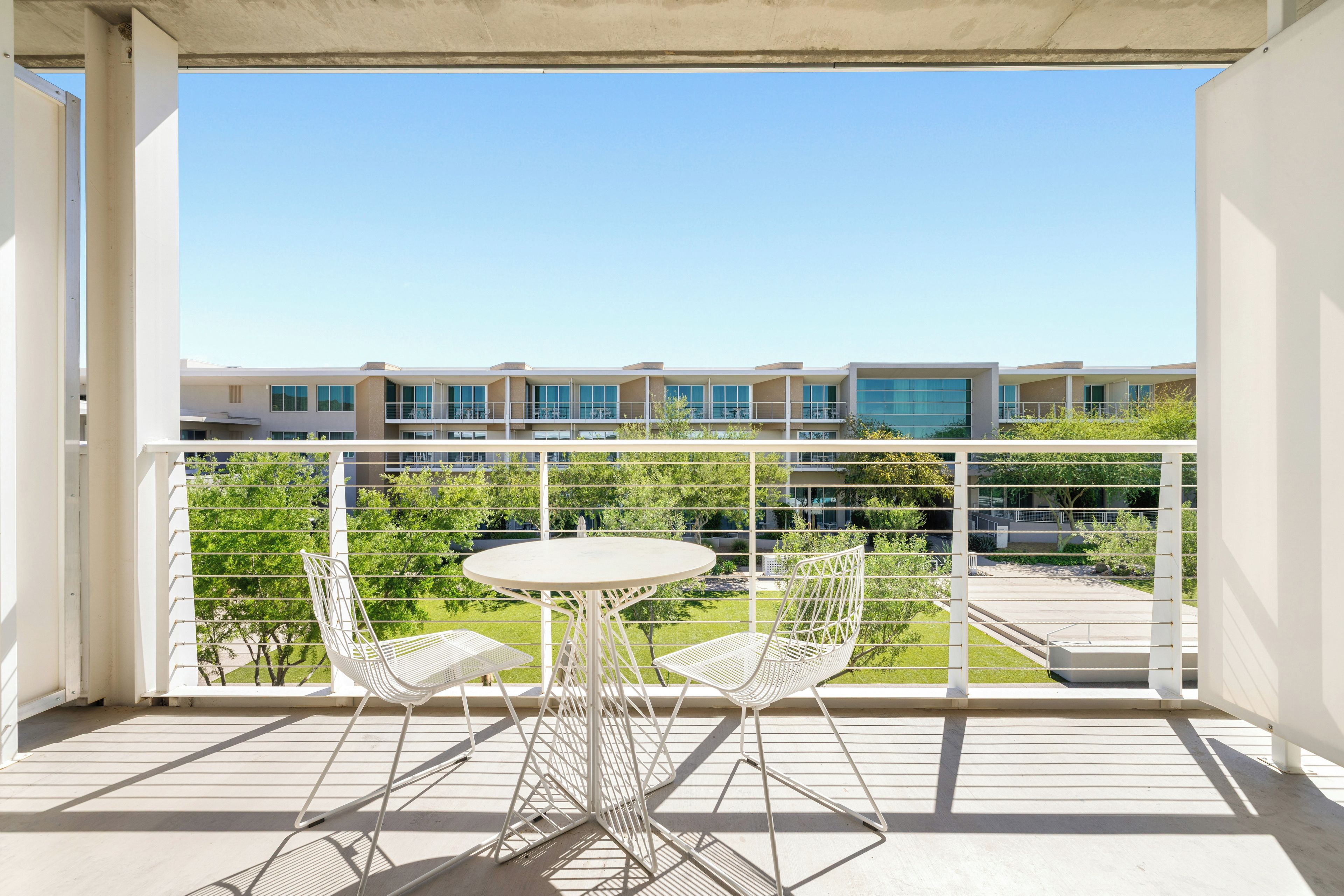 A balcony with a table and two chairs, overlooking a residential area with modern buildings.