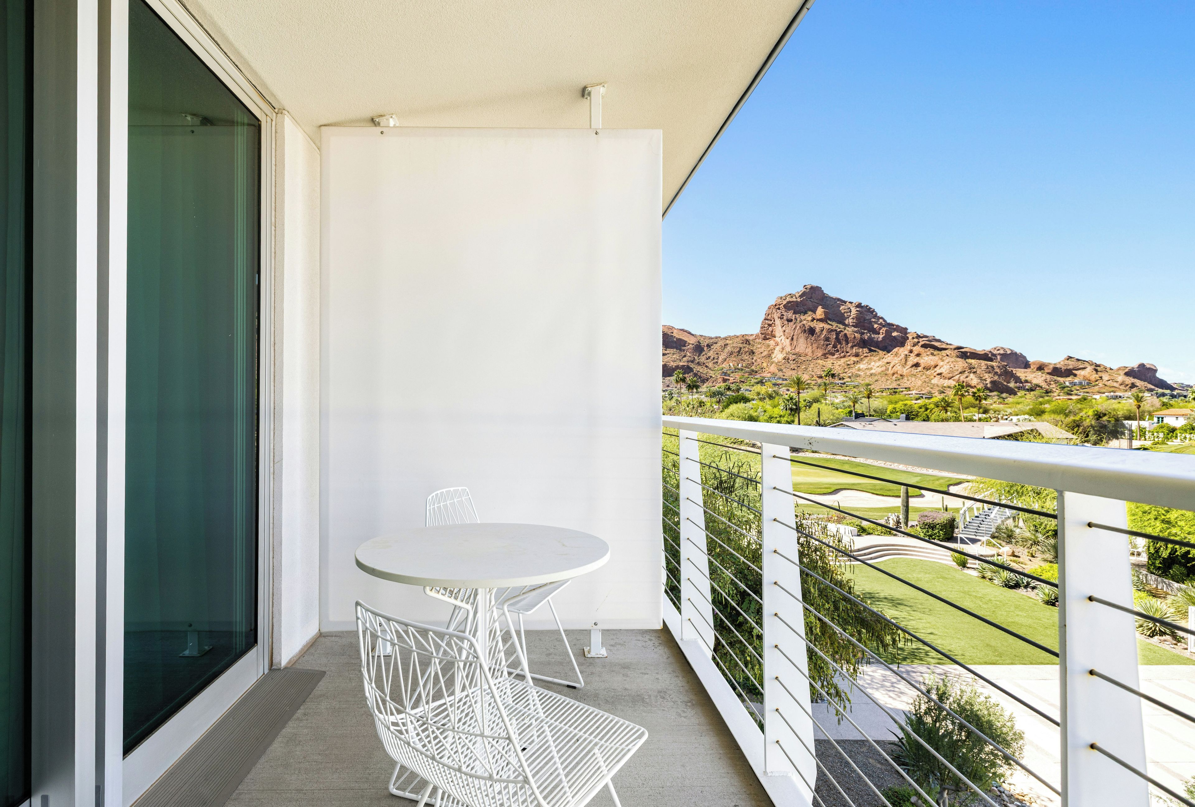 A balcony with a white table and chair, a view of a mountainous landscape, and a clear sky.