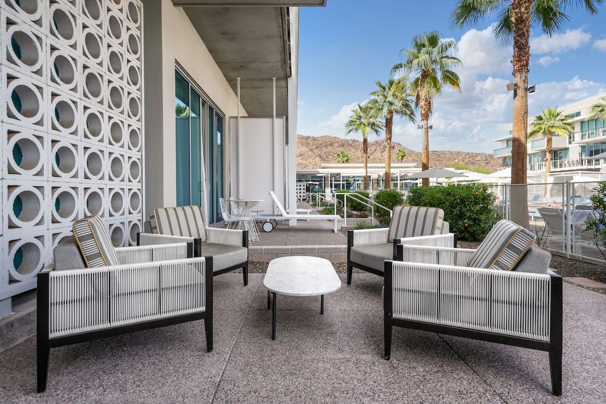 A patio area with wicker furniture and a central table, surrounded by a white decorative wall with circular cutouts.