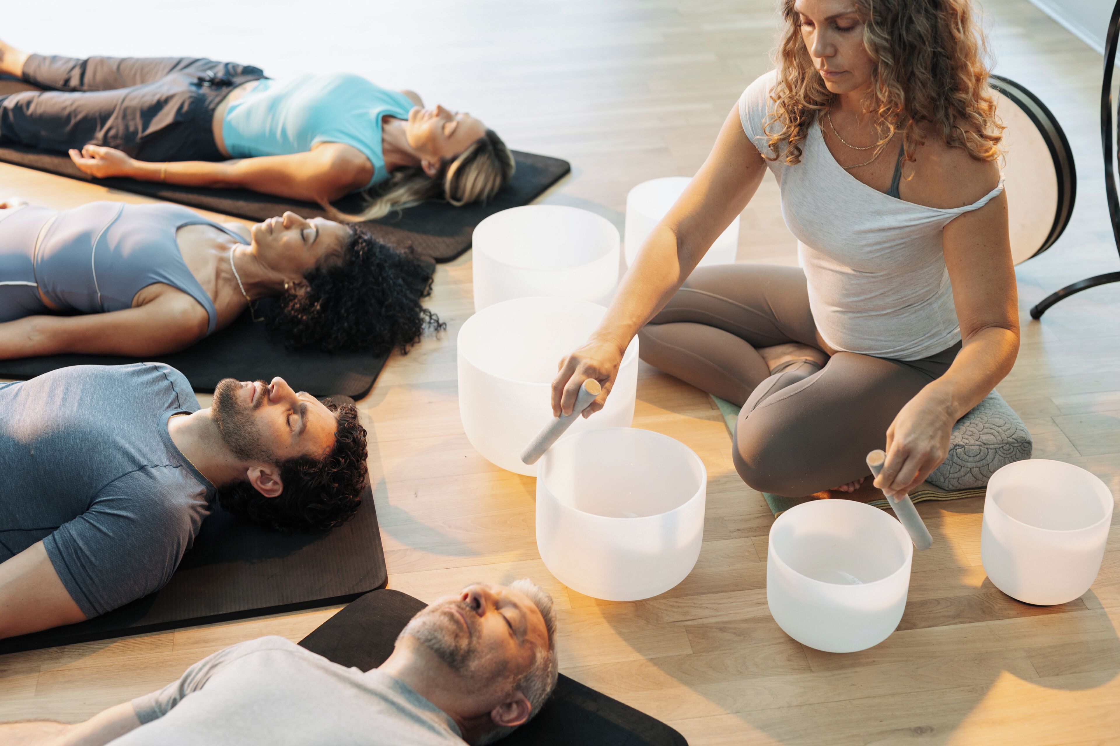 A group of people lying on mats in a room with large white bowls.