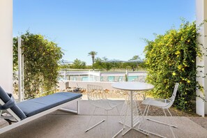 A balcony with a lounge chair, a small round table, and chairs. There is a pool in the background. - Mountain Shadows Resort Scottsdale (Paradise Valley)