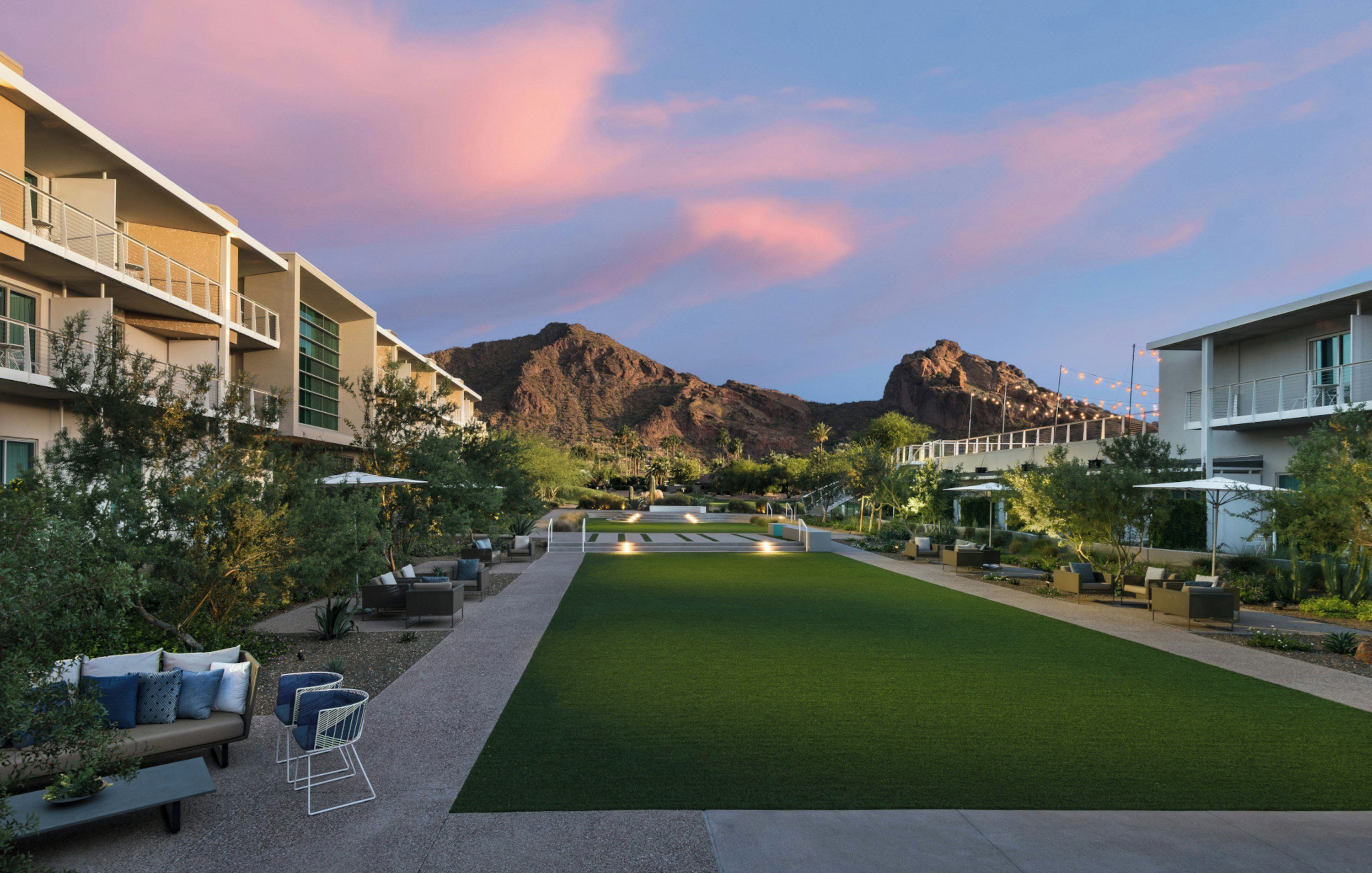 A hotel courtyard with a lawn, outdoor seating, and mountain views.