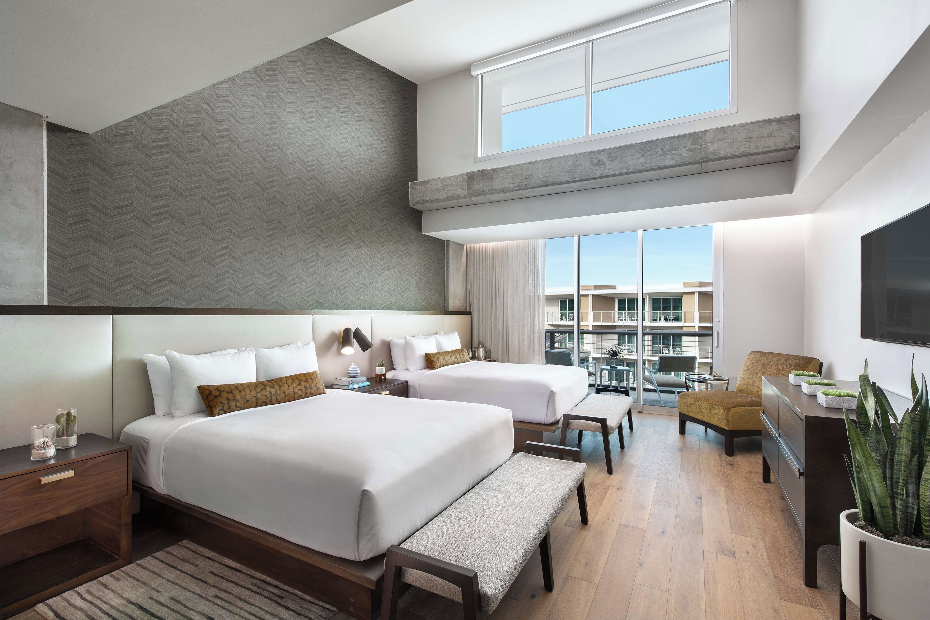 A modern hotel room with two beds, a seating area, and a balcony with a view.