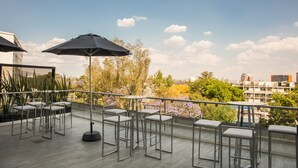 A rooftop terrace with outdoor seating, including tables and chairs, and a large umbrella providing shade. - One Guadalajara Expo (Guadalajara)