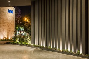 A modern building entrance with a 'one' sign, vertical light panels, and a well-lit pathway.