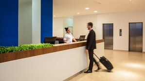 A hotel reception area with a receptionist, a counter, and an elevator. - One Guadalajara Expo (Guadalajara)
