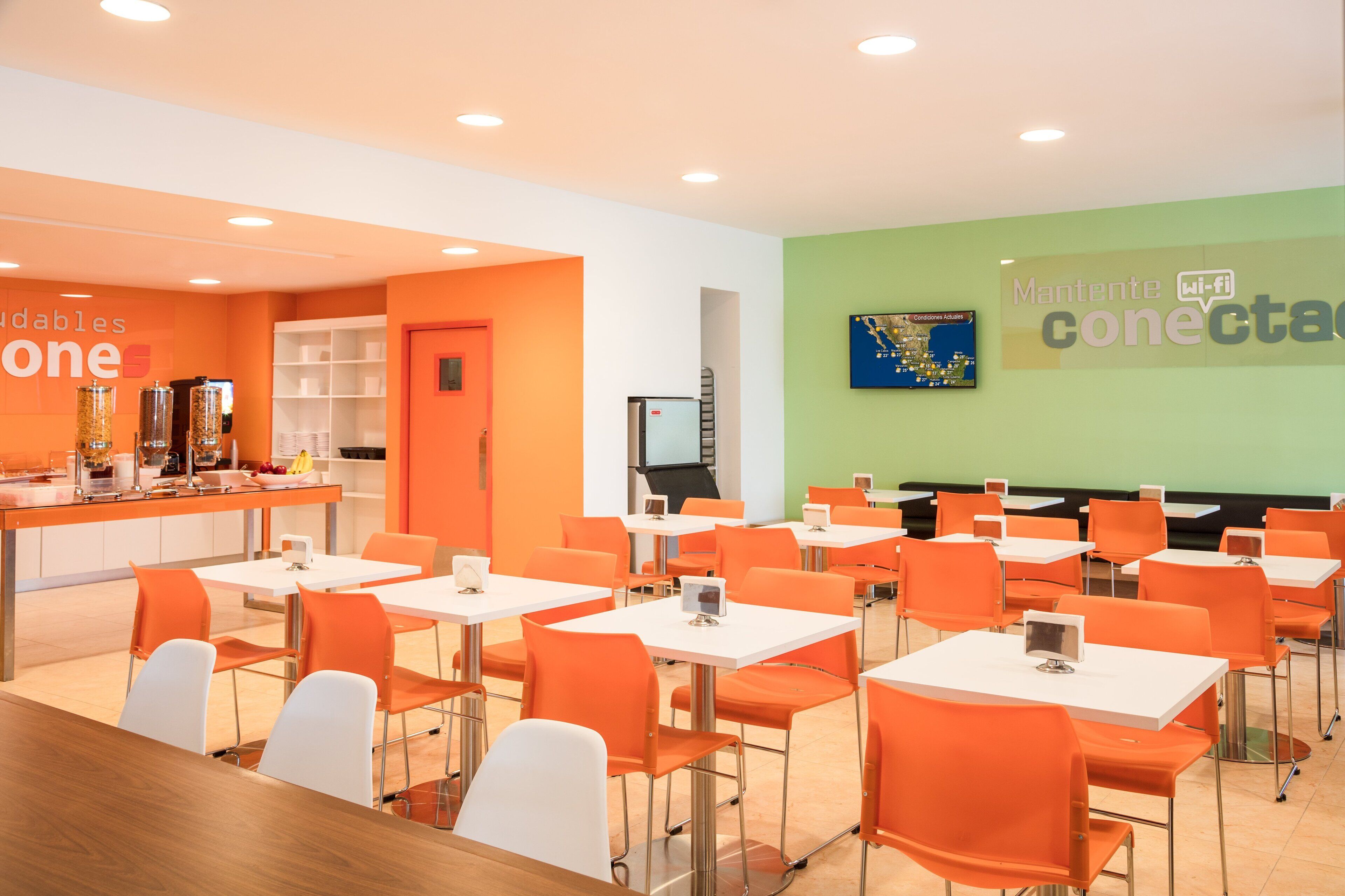 Un comedor moderno con sillas naranjas y mesas blancas, una barra de buffet y un mapa colgado en la pared.