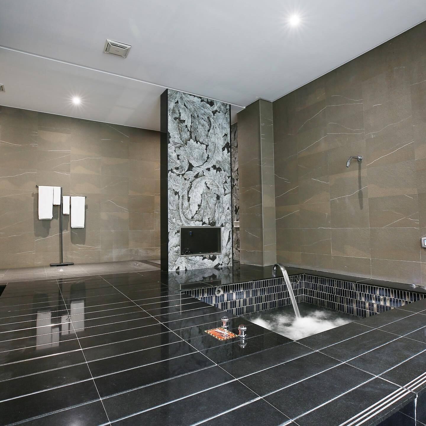 Een moderne badkamer met een vloer van zwarte tegels, een marmeren wand en een douchehoek.