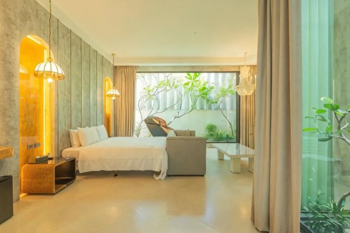 A modern bedroom with a bed, a sofa, a glass partition, and a view of greenery.