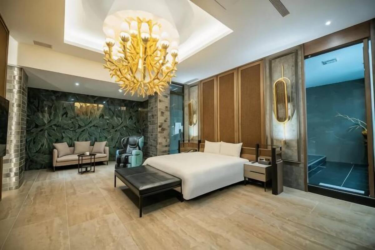 A modern bedroom with a large bed, a sofa, a desk, and a chandelier.