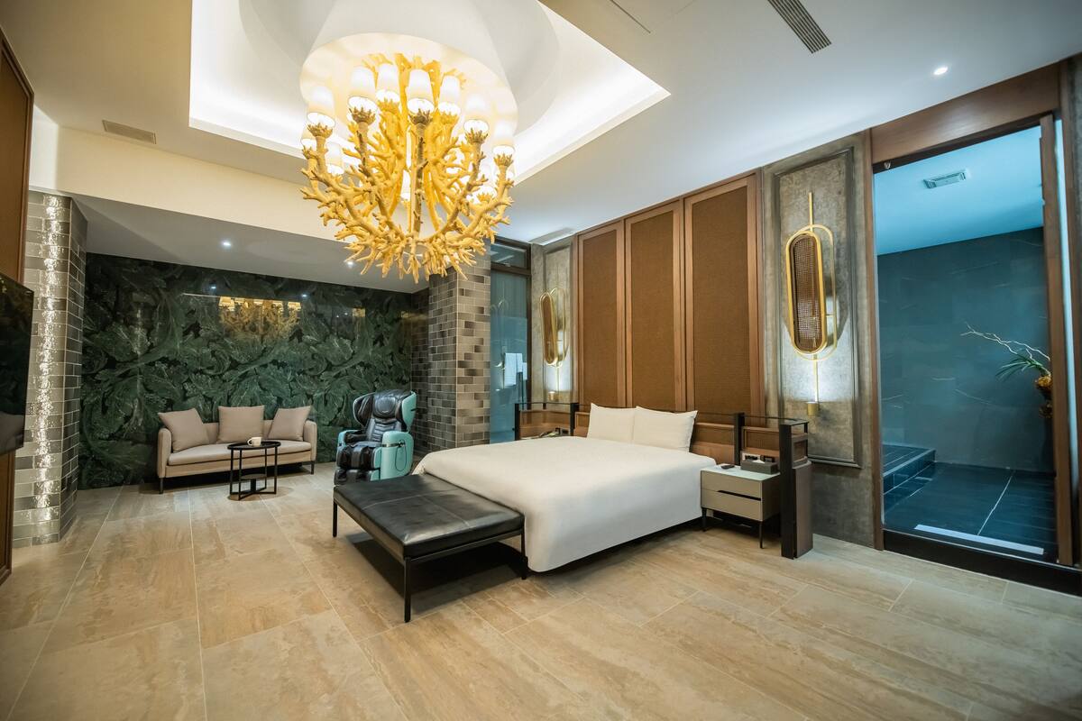A modern bedroom with a large bed, a bench, a sofa, and a decorative chandelier.