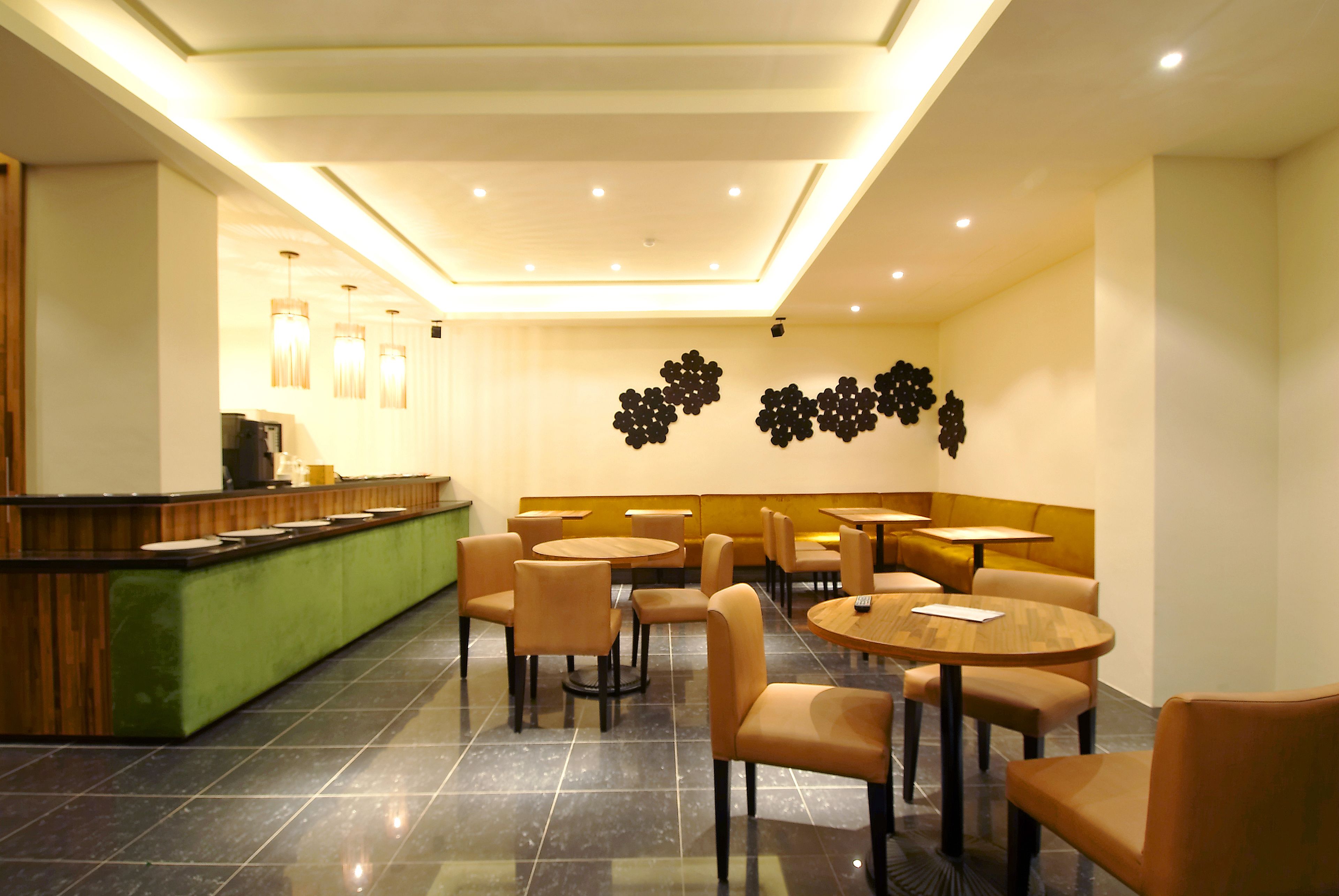 A modern restaurant with a green counter, round tables, and beige chairs.