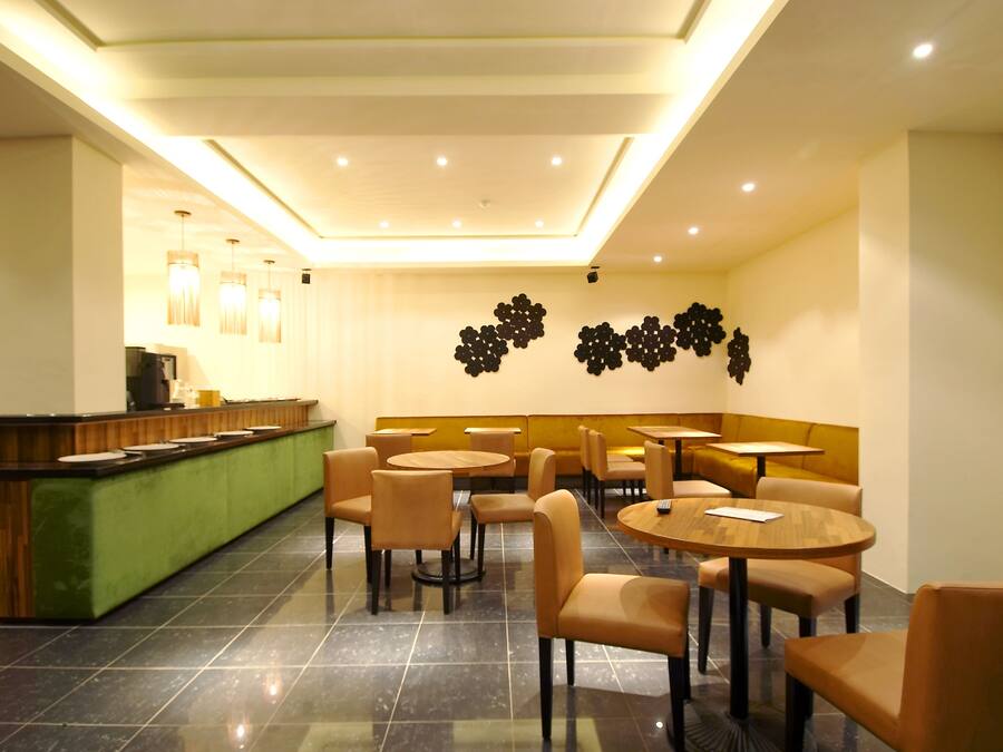 A modern restaurant with a green counter, round tables, and beige chairs.