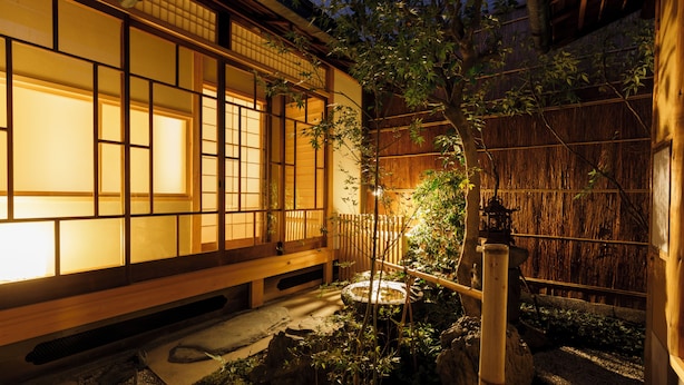 Un edificio japonés tradicional con suelo de esteras de tatami, un banco de madera y un pequeño jardín con rocas y plantas.