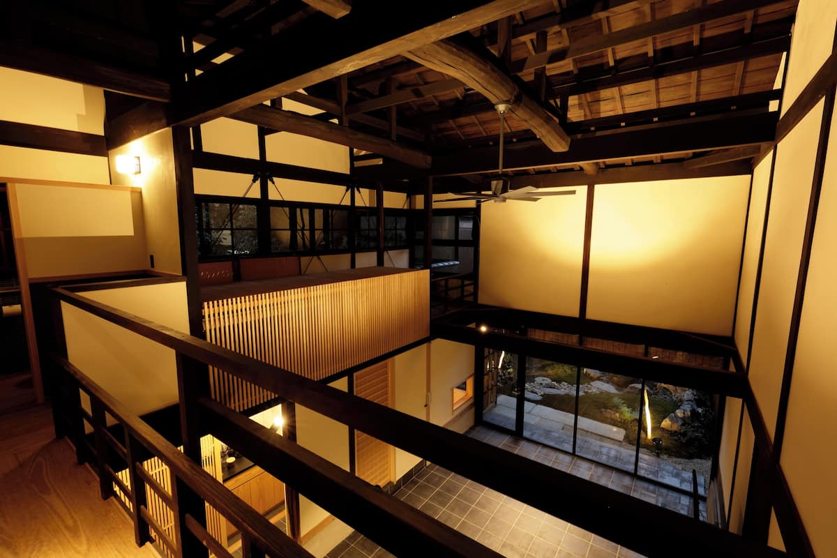 Ein mehrgeschossiges Interieur mit Holzbalken, Tatami-Böden und Blick auf einen Garten.