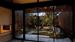 Un interior moderno con un portón de cristal corredizo que da a un jardín con rocas, una valla de madera y un sendero de piedra.