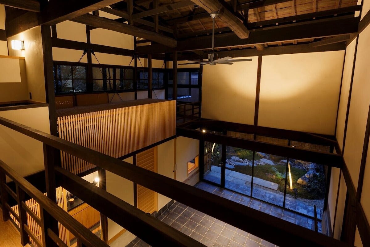 Ein mehrstöckiges Interieur mit Holzbalken, Tatami-Böden und großen Fenstern mit Blick ins Freie.