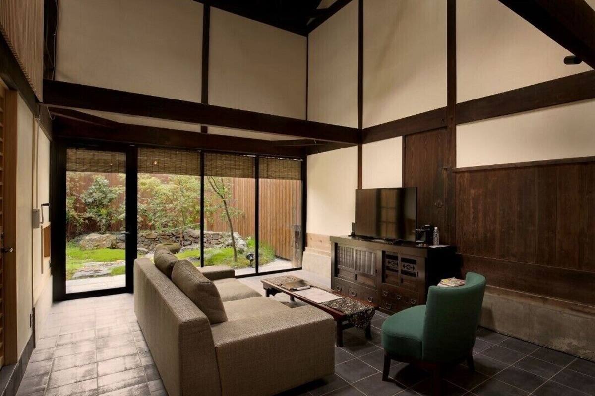 Ein traditioneller japanischer Raum mit Tatami-Bodenbelag, niedriger Holzbalkendecke, einer Tatami-Matratze als Sitzgelegenheit, einem grünen Sessel, einem kleinen Tisch und einem eingebauten Fernseher.