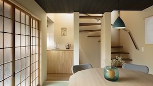 A traditional Japanese-style room with tatami flooring, a low table with chairs, a sliding door with a grid pattern, and a staircase with wooden beams. - Nakano-an (Kyoto)