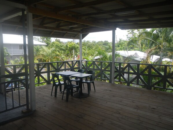 A covered outdoor area with a wooden deck, metal railing, and a table with chairs. - Samoa Sport Lodge (Apia)
