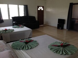 A hotel room with two beds, a sofa, a TV, and a door with a window. - Samoa Sport Lodge (Apia)