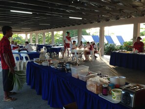 A covered outdoor dining area with tables and chairs, food service staff, and a buffet setup. - Samoa Sport Lodge (Apia)