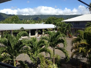 A building with a covered outdoor area, surrounded by palm trees and greenery, with a mountainous backdrop. - Samoa Sport Lodge (Apia)