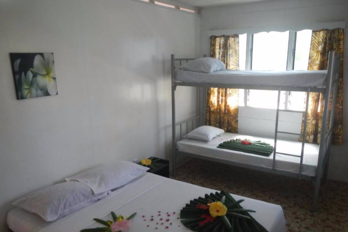 A single bed with a decorative floral arrangement, a bunk bed with a window, and a painting on the wall.